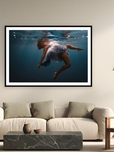 Black wood frame fine art print of Water Ballet by Sarah Swan, St. John, USVI, displayed on a modern living room wall — maddie is a ballet dancer who came to Sarah with the idea of shooting underwater — the Caribbean turned choreography into something else entirely.