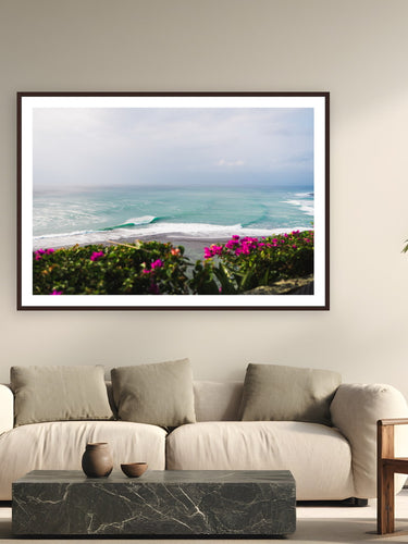 Black wood frame fine art print of From The Cliffs by Ben Gamlin, Bingin, Bali, displayed on a modern living room wall — bougainvillea, reef, and a dropping tide above Bali's Bingin Beach.