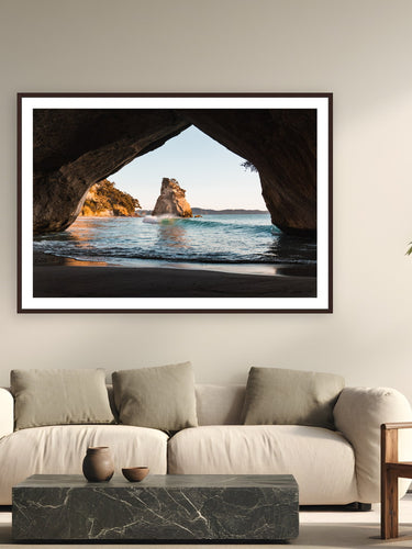 Black wood frame fine art print of The Arch by Ben Gamlin, Cathedral Cove, Coromandel Peninsula, New Zealand, displayed on a modern living room wall — cathedral Cove at first light, framed through its namesake arch.