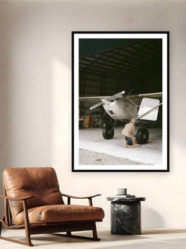 Black wood frame fine art print of Alaskan Transpo by Brooklyn Phillips, McCarthy, Alaska, displayed on a reading nook wall — mcCarthy, Alaska — a town of about two dozen winter residents, where bush planes replace cars and a hand-drawn map counts as GPS.