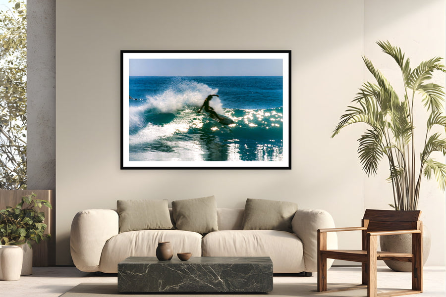 Black wood frame fine art print of Backlit Slide by Devon Cardamone, Malibu, California, displayed on a modern living room wall — late-afternoon Malibu, when the sun drops behind the lineup and punches straight through each wave as it feathers.