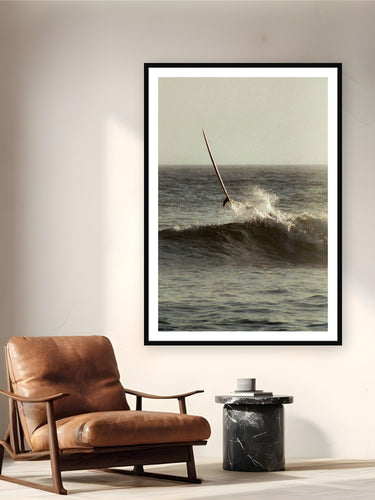 Black wood frame fine art print of Ghost Rider by Devon Cardamone, San Onofre, CA, displayed on a reading nook wall — a longboard launches skyward at San Onofre — the cobblestone break where Southern California surf culture took root in the 1930s.
