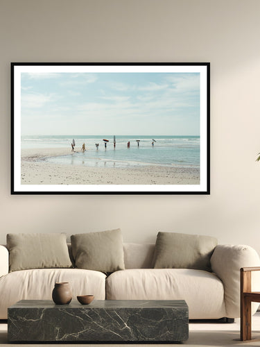 Black wood frame fine art print of Friends and Boards by Sarah Swan, Mexico, displayed on a modern living room wall — no waves, no problem — a lineup of friends and boards at the water's edge on a flat afternoon in Mexico.